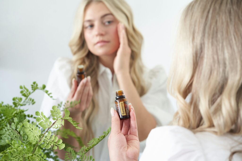 A woman applies natural face oil in front of a mirror, surrounded by green plants.